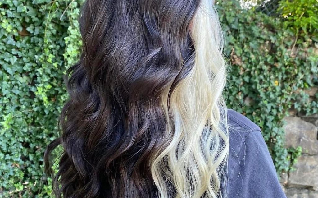 A woman with long, wavy hair is smiling, showcasing her flowing locks in a bright, natural setting.