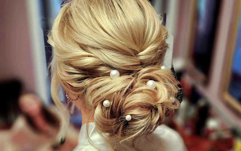 A woman with blonde hair styled in a bun, adorned with elegant pearls, exuding sophistication and grace.