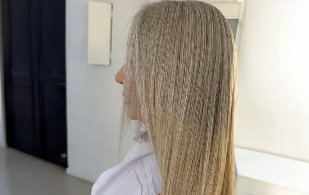 Close up view of a woman's blonde straight hair. We see her from her left profile.