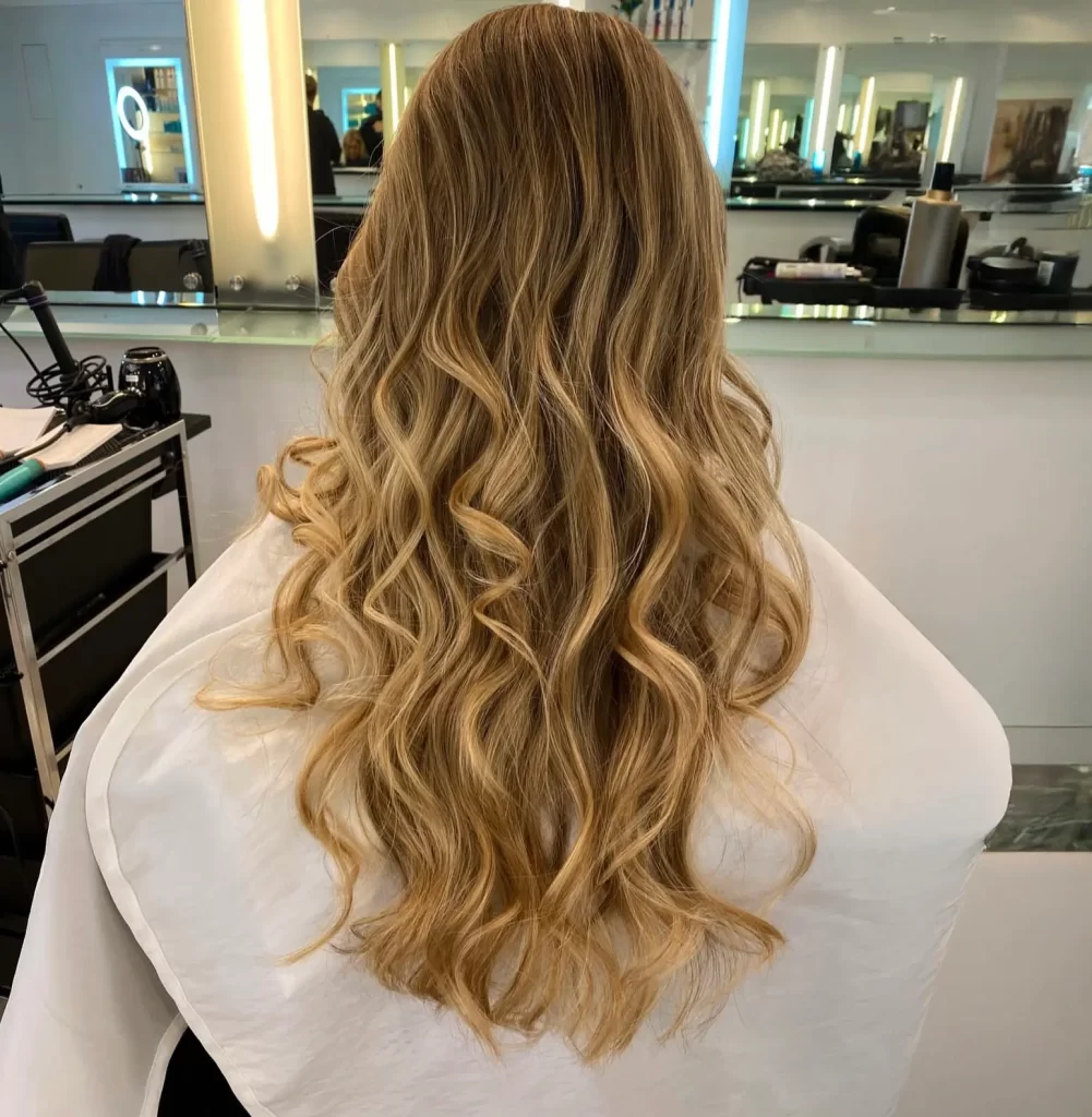 Close up view of a woman's blonde wavy hair. She is sitting in a chair with her back to us.